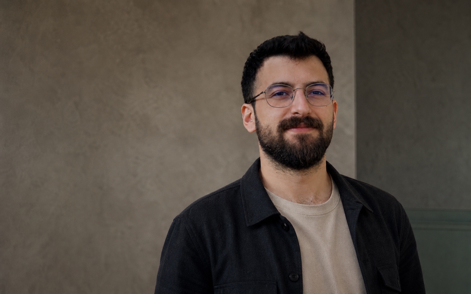 Portrait of Çağrı Bozgeyik in a charcoal overshirt against a warm neutral background